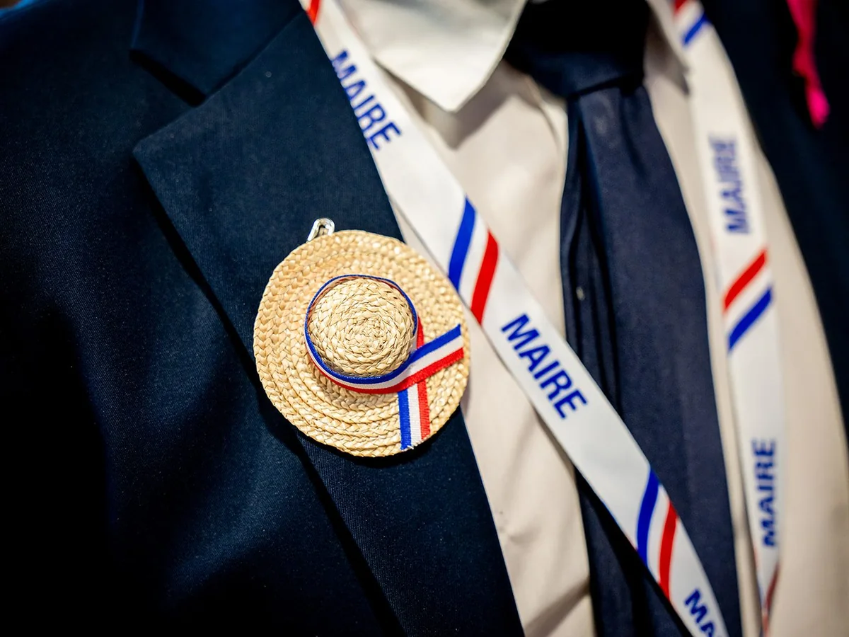 Cordon bleu, blanc et rouge « MAIRE » et mini-chapeau de paille à ruban tricolore sur le revers d’un Maire au Salon des Maires