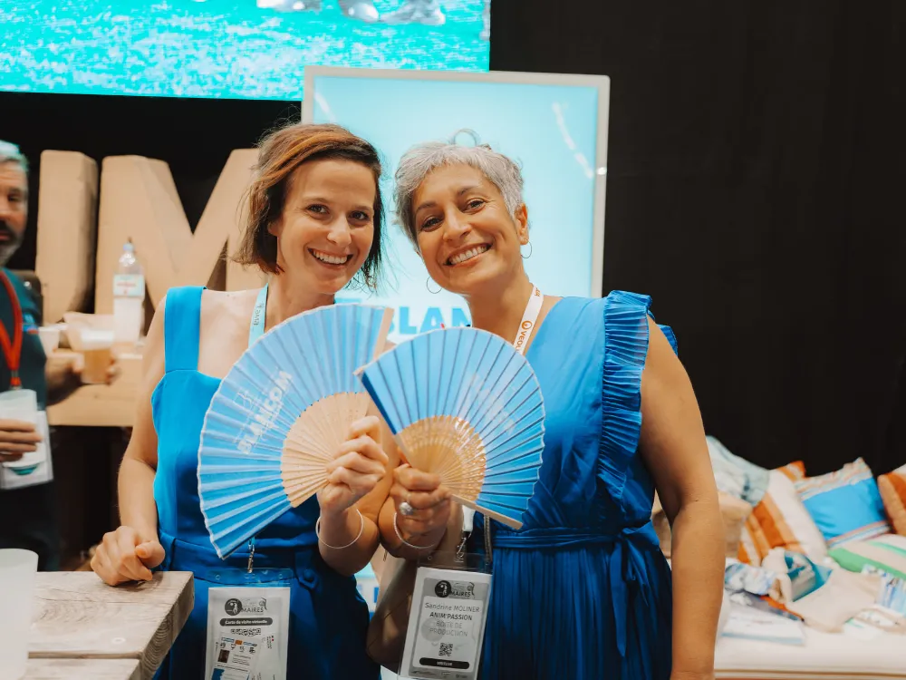 Exposantes souriantes avec leurs éventails sur leur stand du Salon des Maires des Pyrénées-Orientales 2026